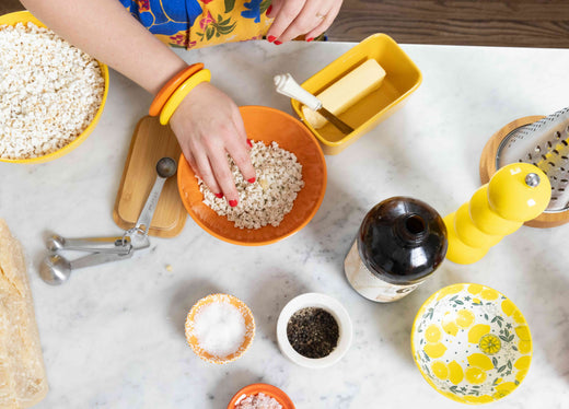 Woman's hand reaching into a bowl of popcorn on a kitchen table with other ingredients