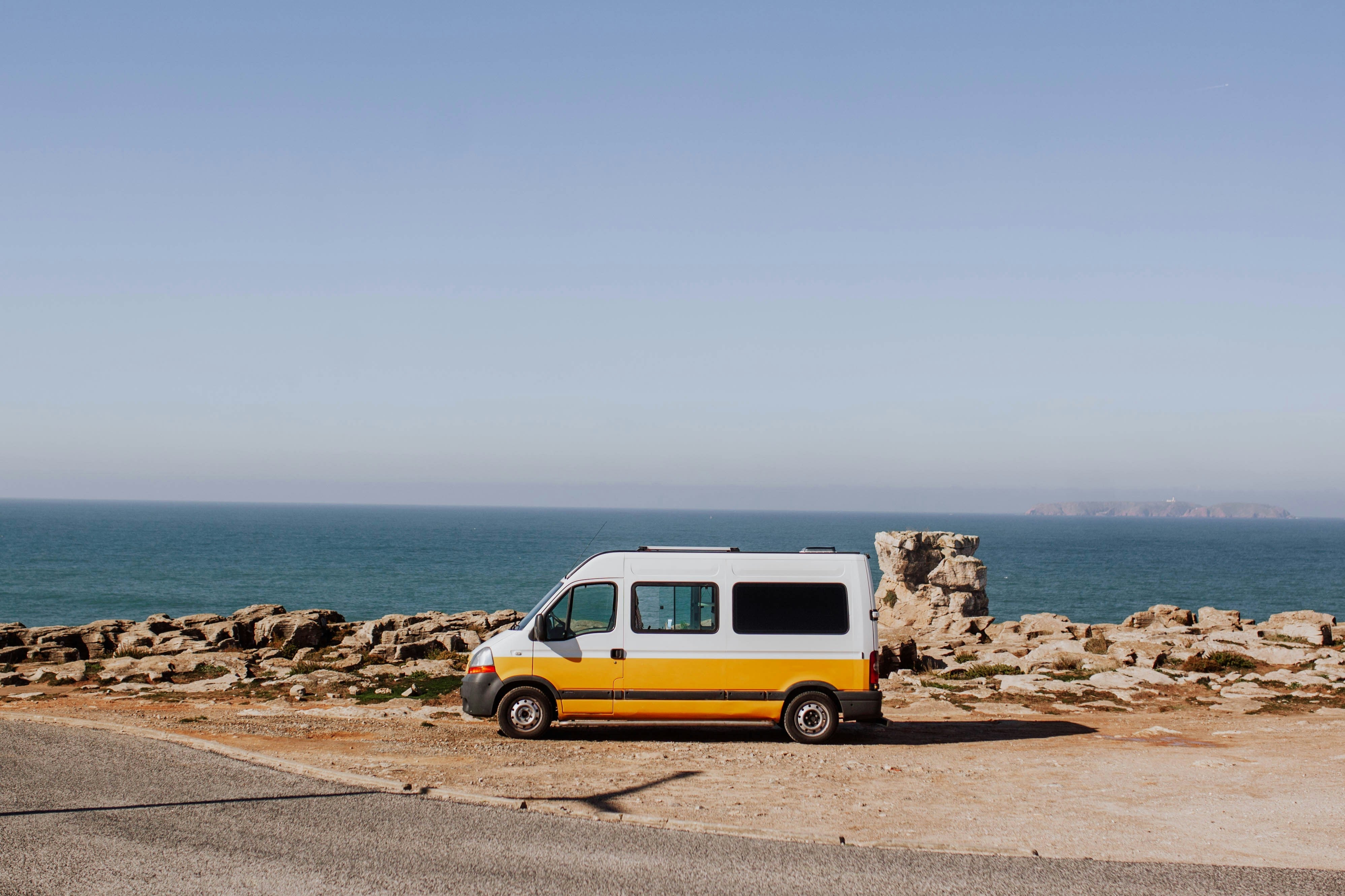 A yellow and white sprinter van is parked by the coast